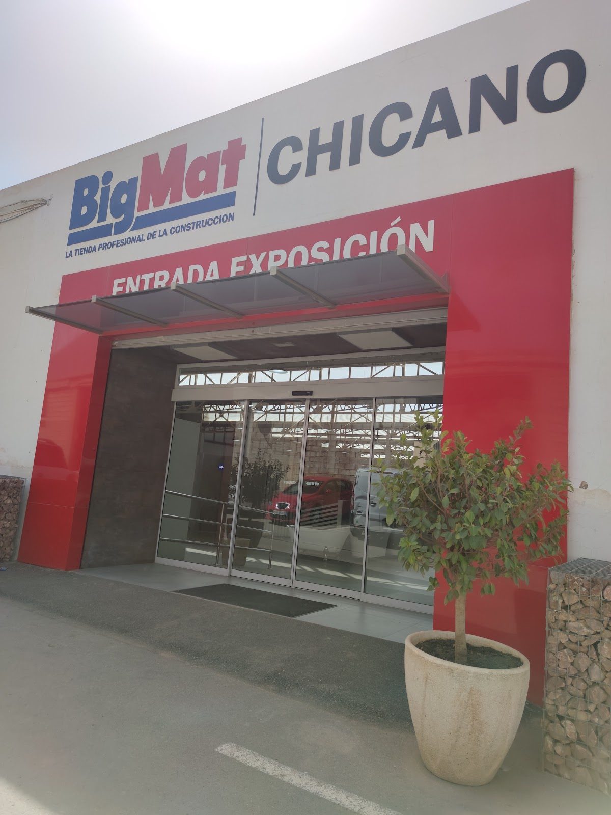 The entrance of BIGMAT CHICANO features a modern facade with red accents and large glass doors.