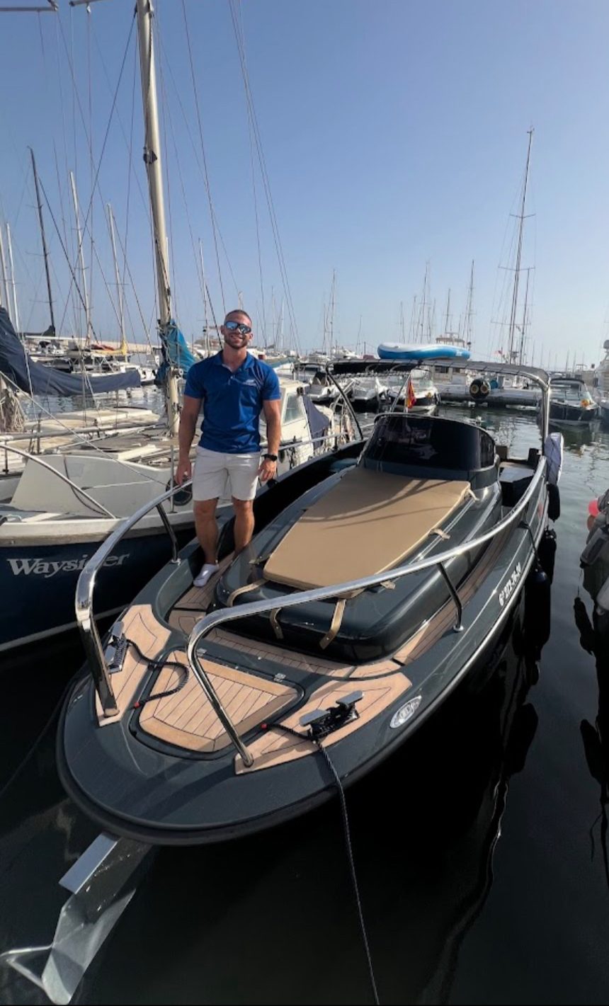 A man stands on a sleek boat at Puerto Deportivo de Estepona, surrounded by other moored boats.