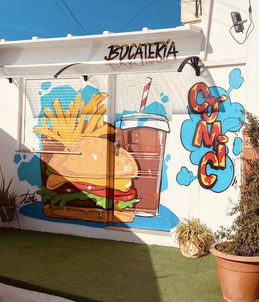Colorful mural featuring a burger, fries, and a drink on the exterior wall of Bocateria Comic in Mollina.
