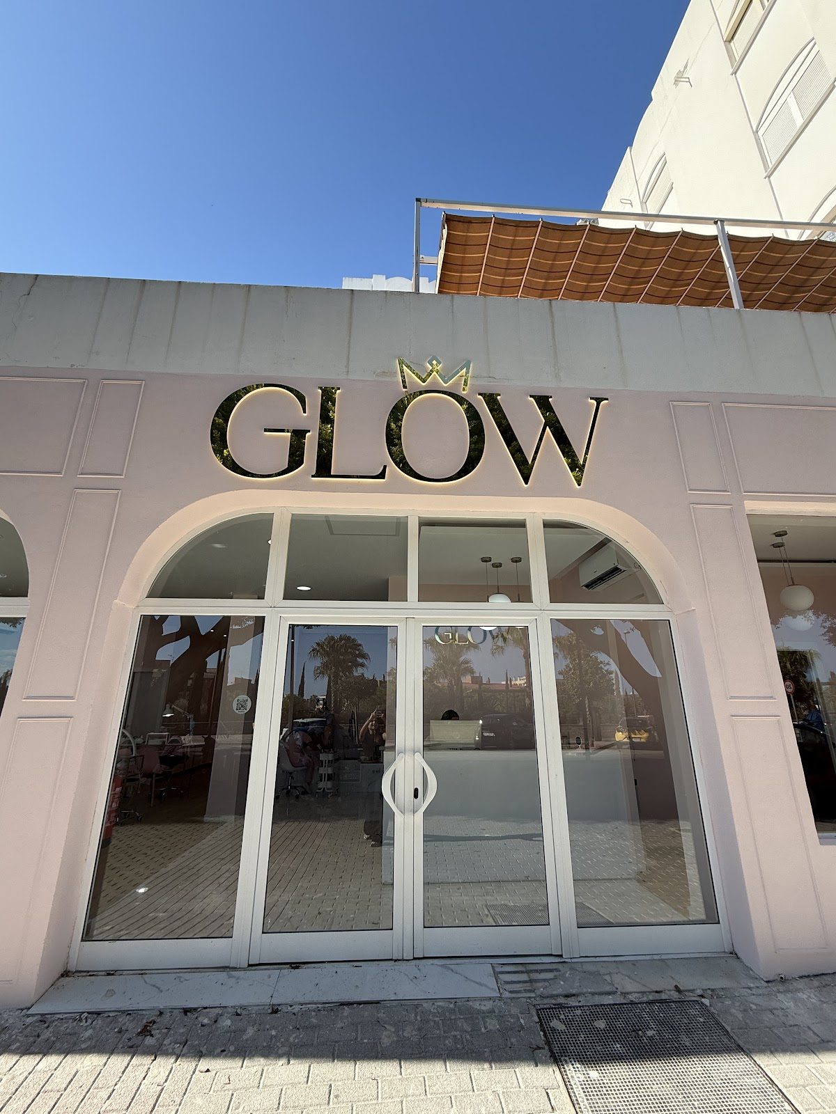 El exterior de By Glow Benalmádena presenta un diseño moderno con grandes puertas de cristal y un llamativo letrero "GLOW".