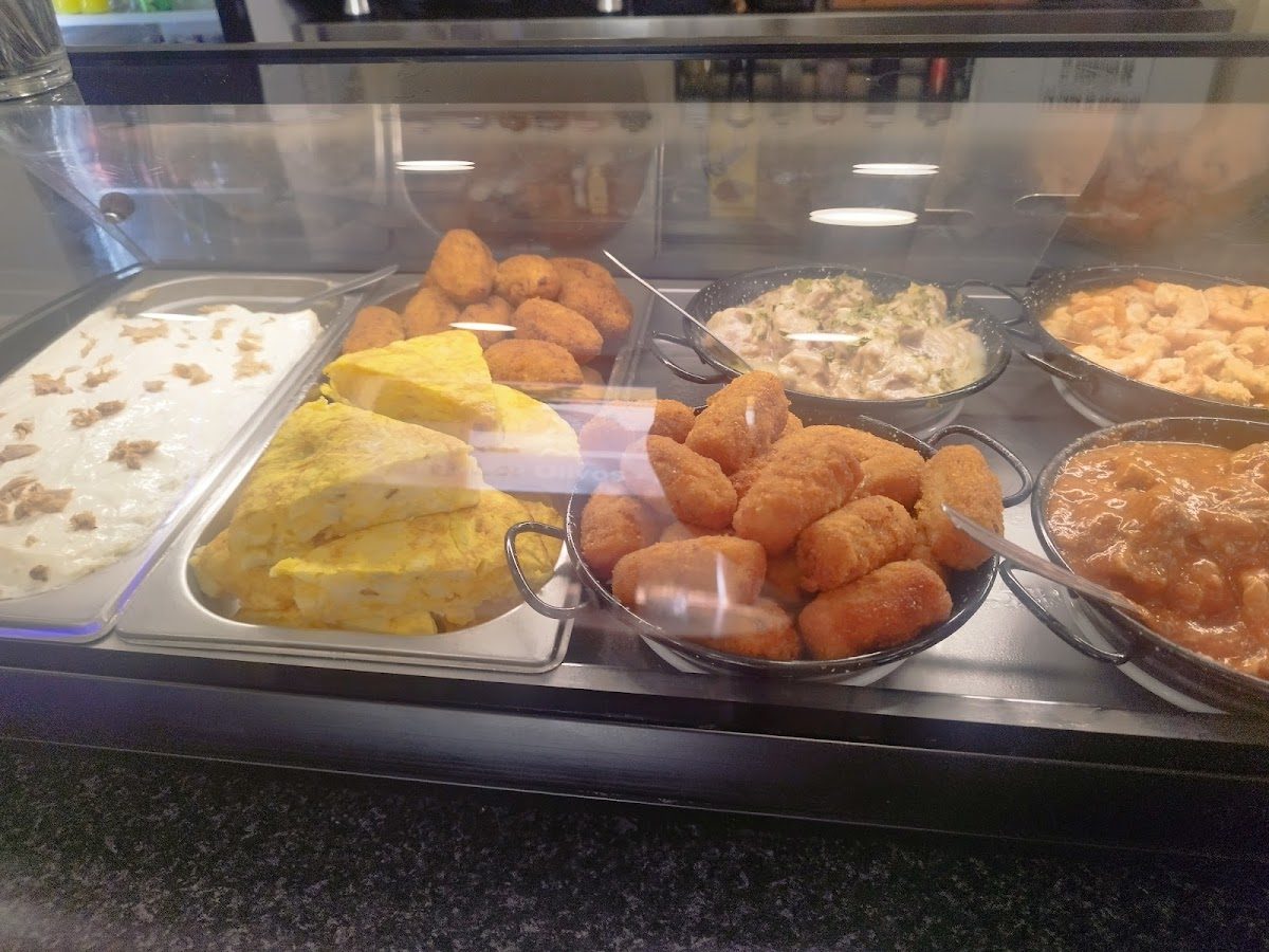 Café Bar Los Olivos displays a variety of tapas, including croquettes and seafood dishes, in a glass showcase.