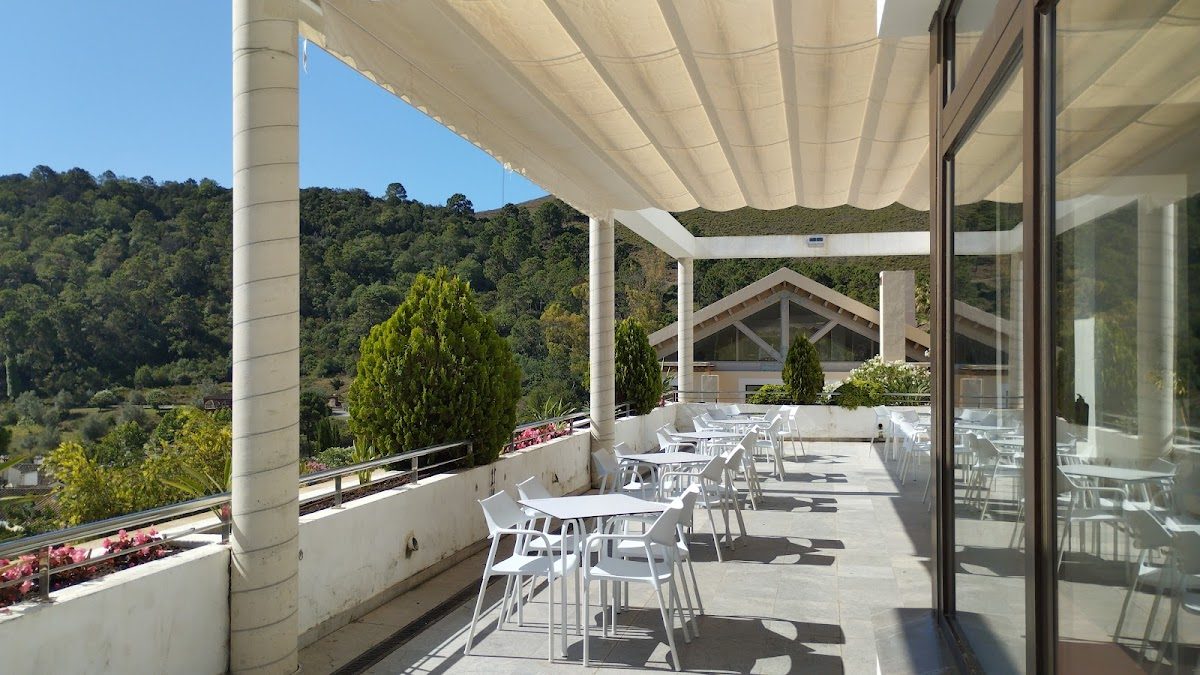 The terrace of Cafe-bar Town Hall features white tables and chairs with a scenic view of greenery.