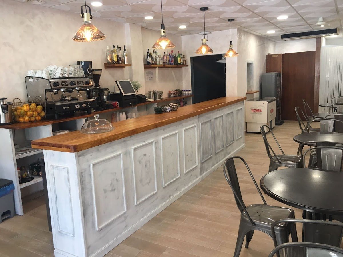 La cafetería La Abuela cuenta con una moderna zona de bar con mostrador de madera y sillas de metal en un interior luminoso.