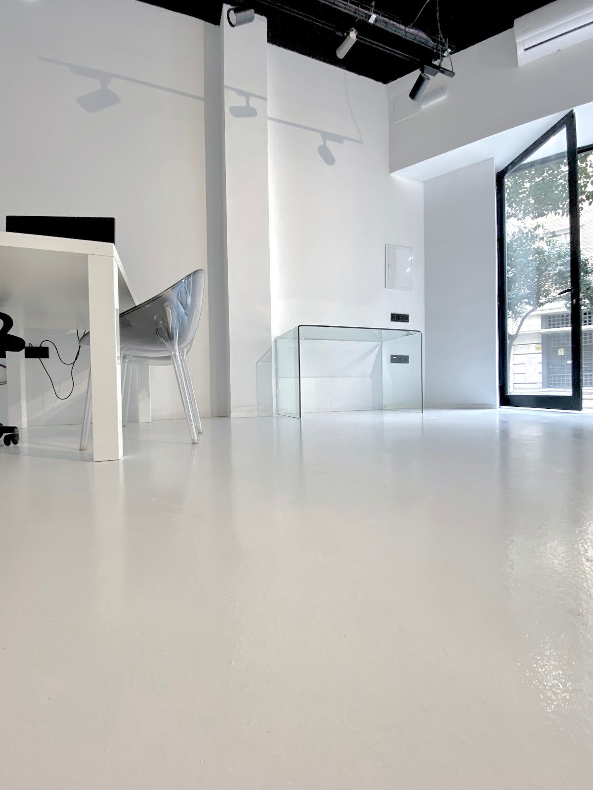 Interior luminoso y minimalista del estudio CAPELLA, con una mesa de cristal y un escritorio con una silla transparente.