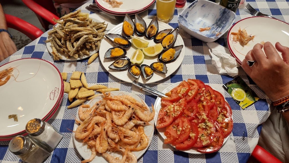 A table set with various seafood dishes, including shrimp, mussels, fried fish, and tomato salad.