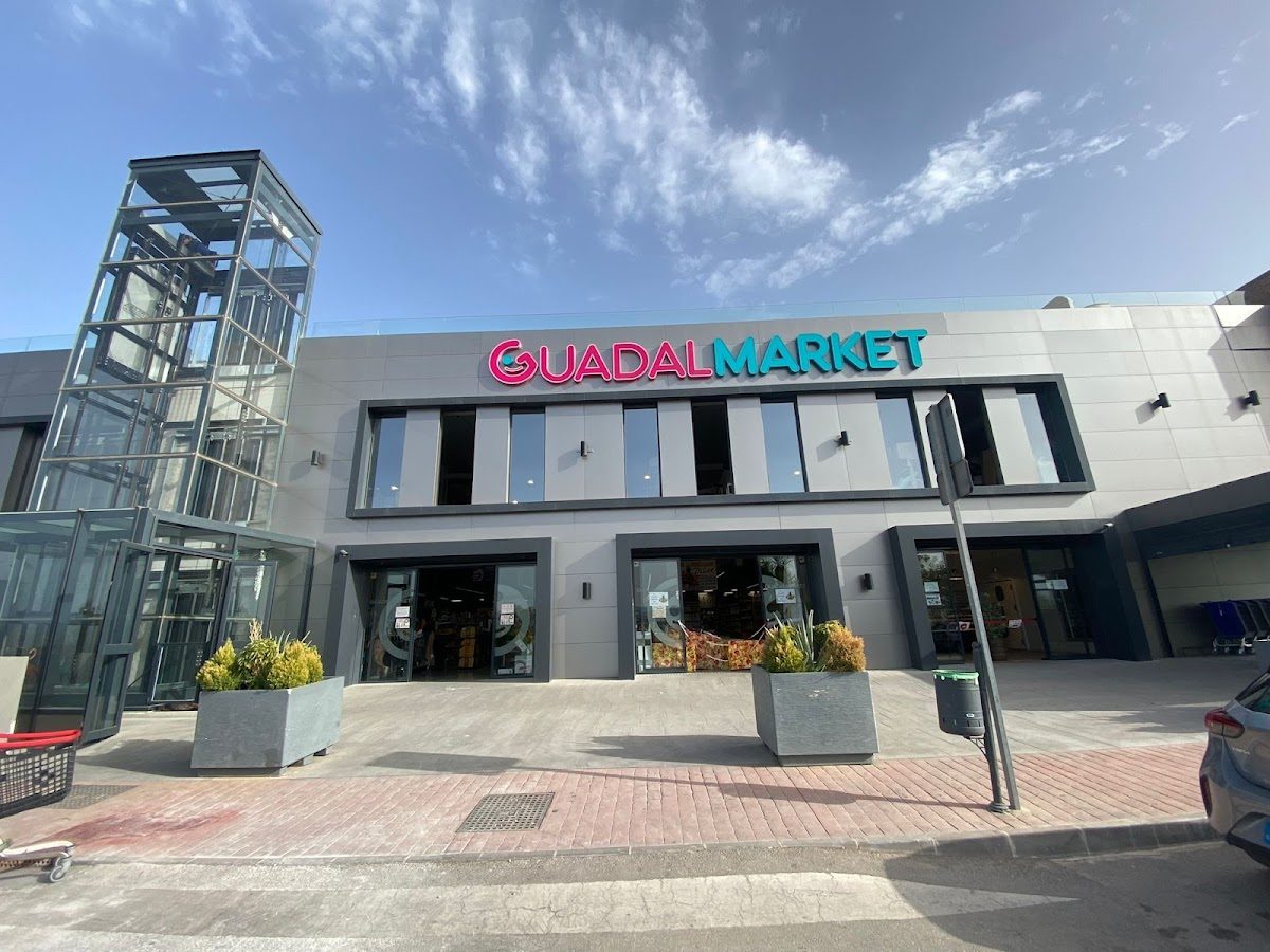 El exterior de Guadalmarket presenta una arquitectura moderna con grandes ventanales de cristal y coloridos letreros.