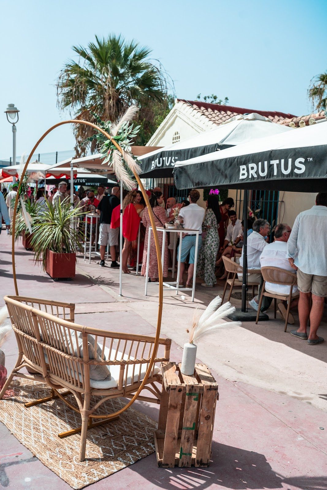 Casaamigos Playa cuenta con mesas al aire libre, con un banco de bambú y palmeras, y está repleta de clientes que disfrutan del ambiente.