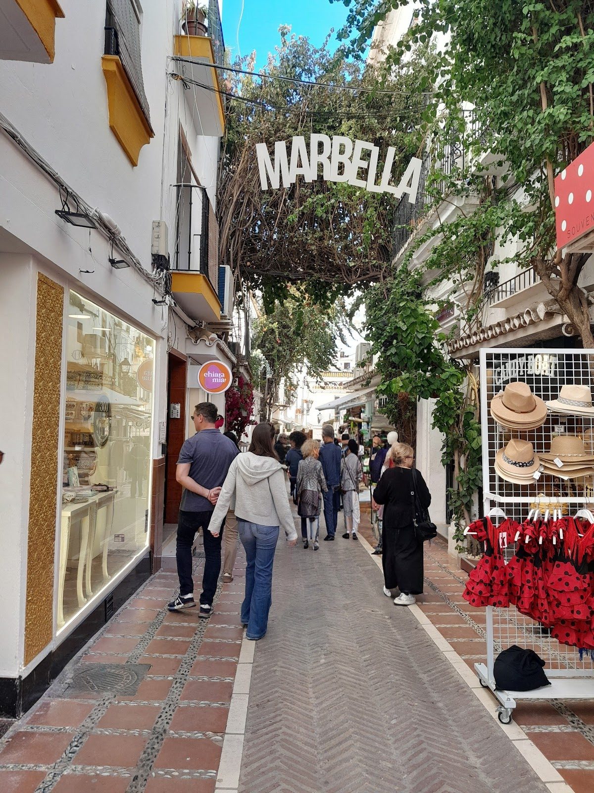 A lively street in Marbella's Casco Antiguo, lined with shops and greenery overhead.