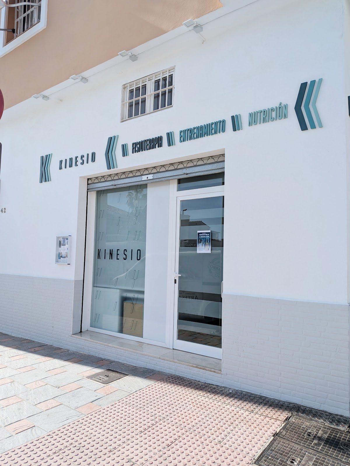 El exterior de CENTRO KINESIO presenta un diseño moderno con una fachada blanca y letreros de color turquesa.