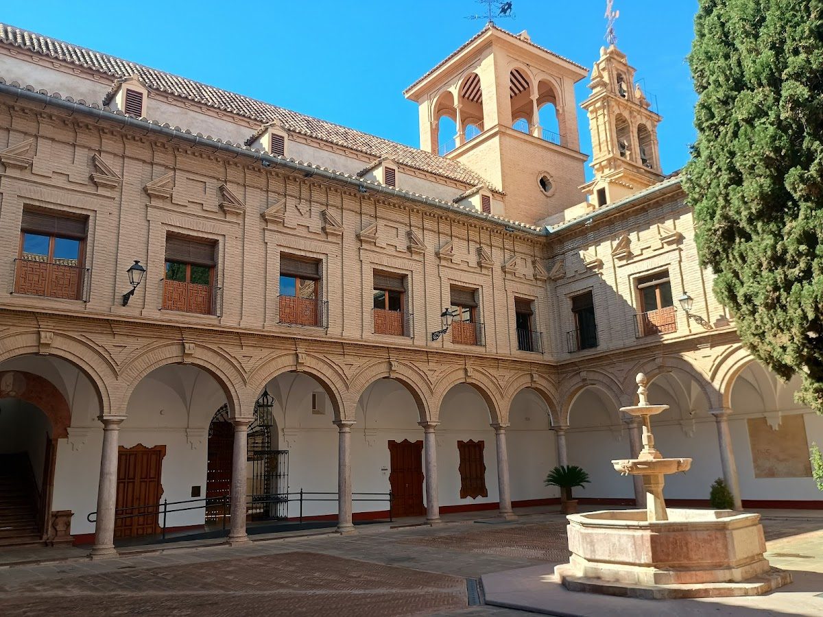 The image shows a historic building with arched columns, a fountain, and a tower, located at City Council Antequera.