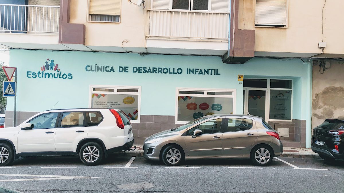 Exterior view of Clínica de Desarrollo Infantil ESTÍMULOS with colorful signage and parked cars outside.