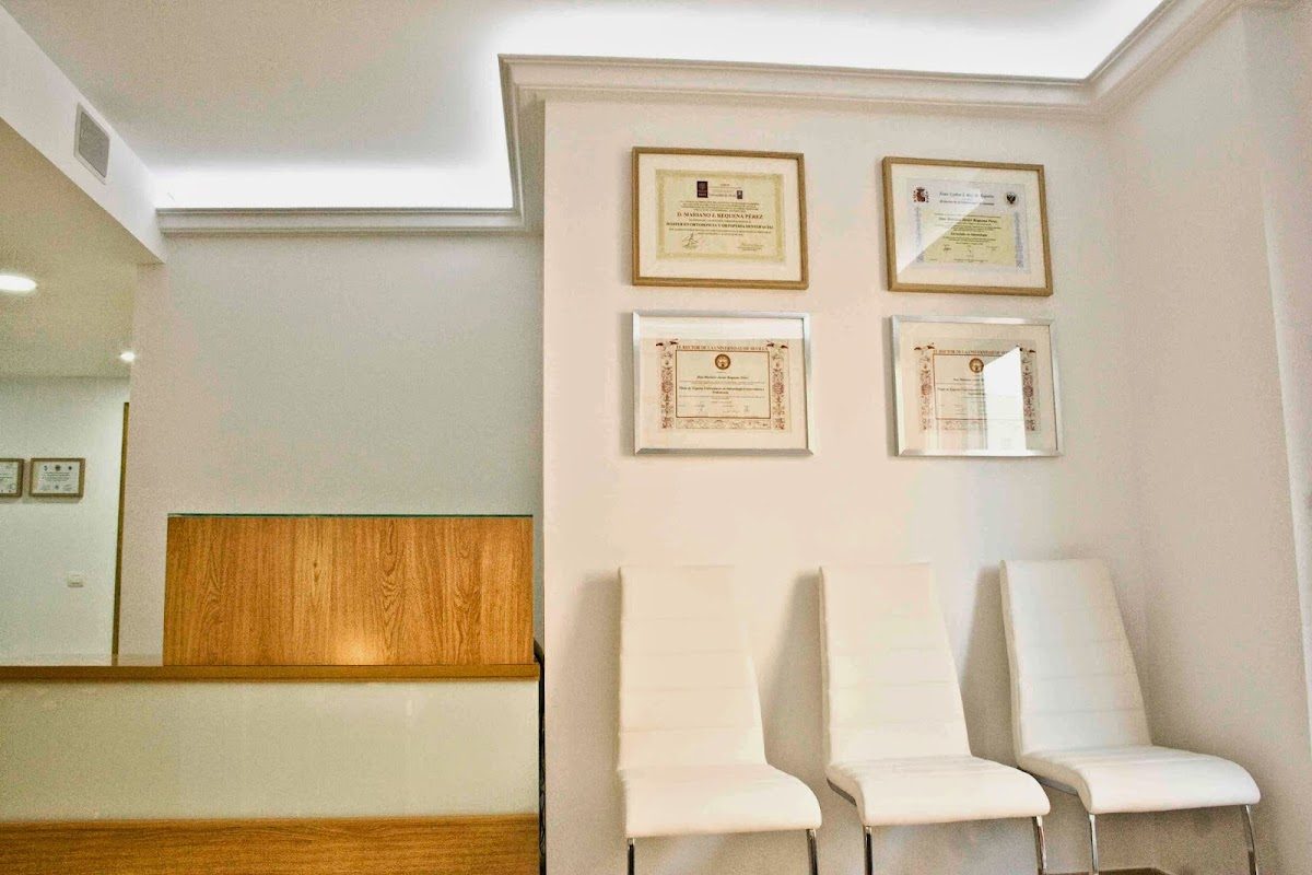Modern waiting area with white chairs and framed certifications at Clinica Dental Mariano Requena in Fuengirola.