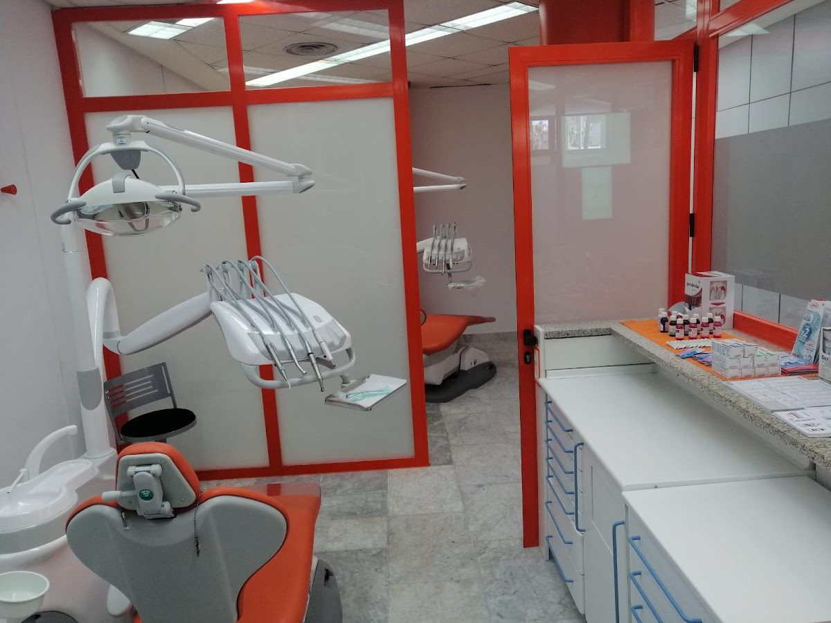 Modern dental clinic interior with orange accents, dental chairs, and equipment visible.