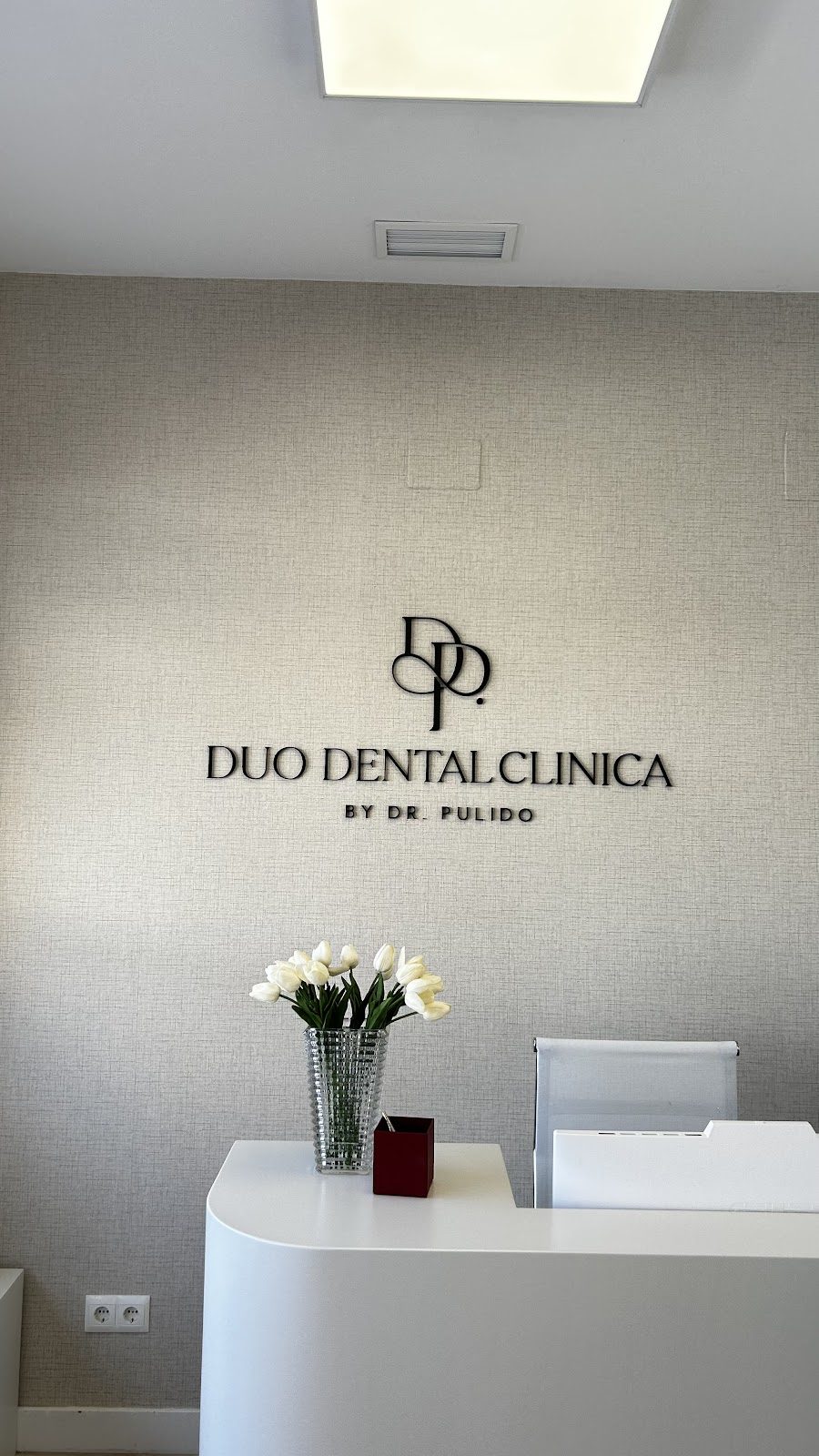 Modern reception area of Clinica Duo Dental Fuengirola with a sleek desk and decorative flowers.