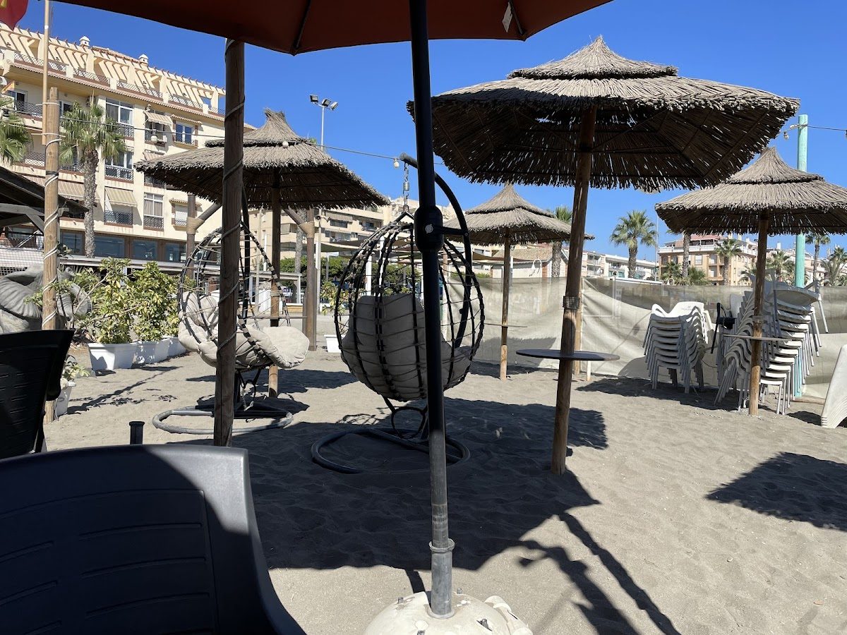 Coctelería Smile Playa features beachside seating with hanging chairs and thatched umbrellas on sandy ground.
