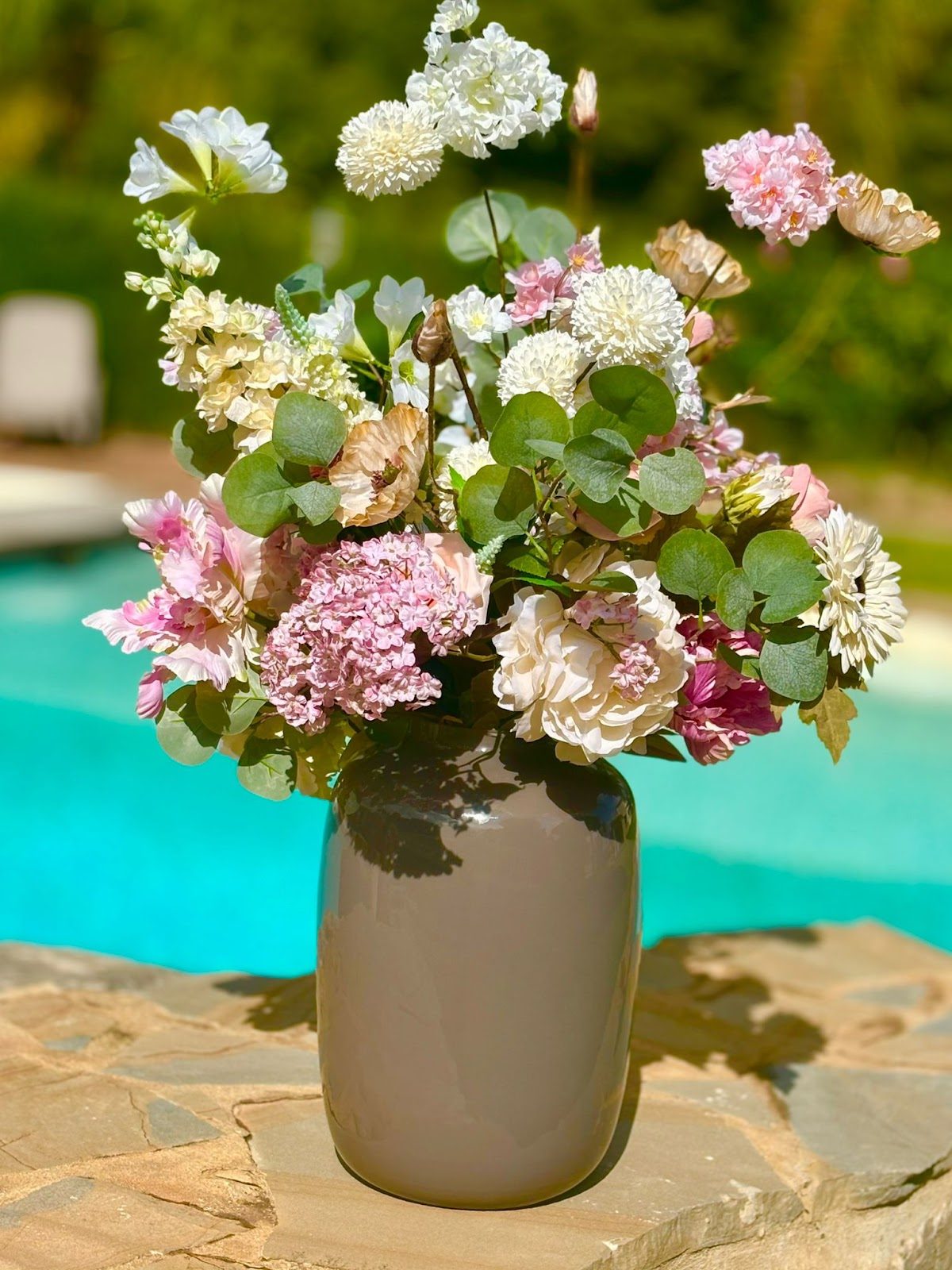Un precioso arreglo floral en tonos pastel en un jarrón gris, colocado junto a la piscina.