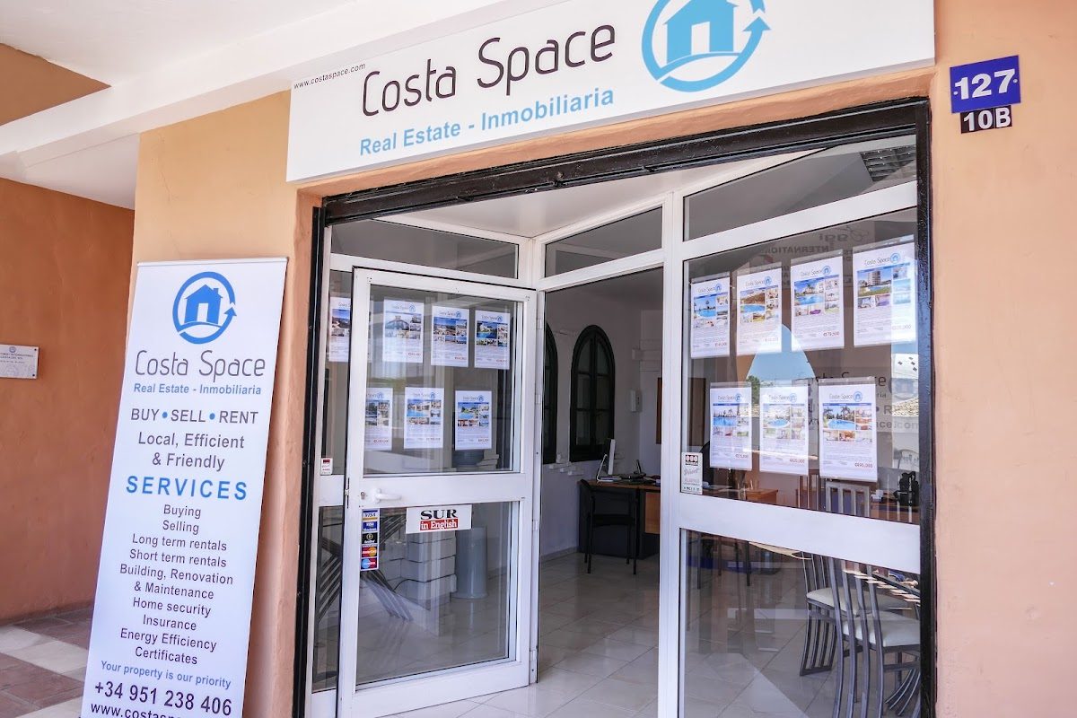 Oficina inmobiliaria de CostaSpace con una entrada de cristal que muestra listados de propiedades y un letrero de servicio en el exterior.