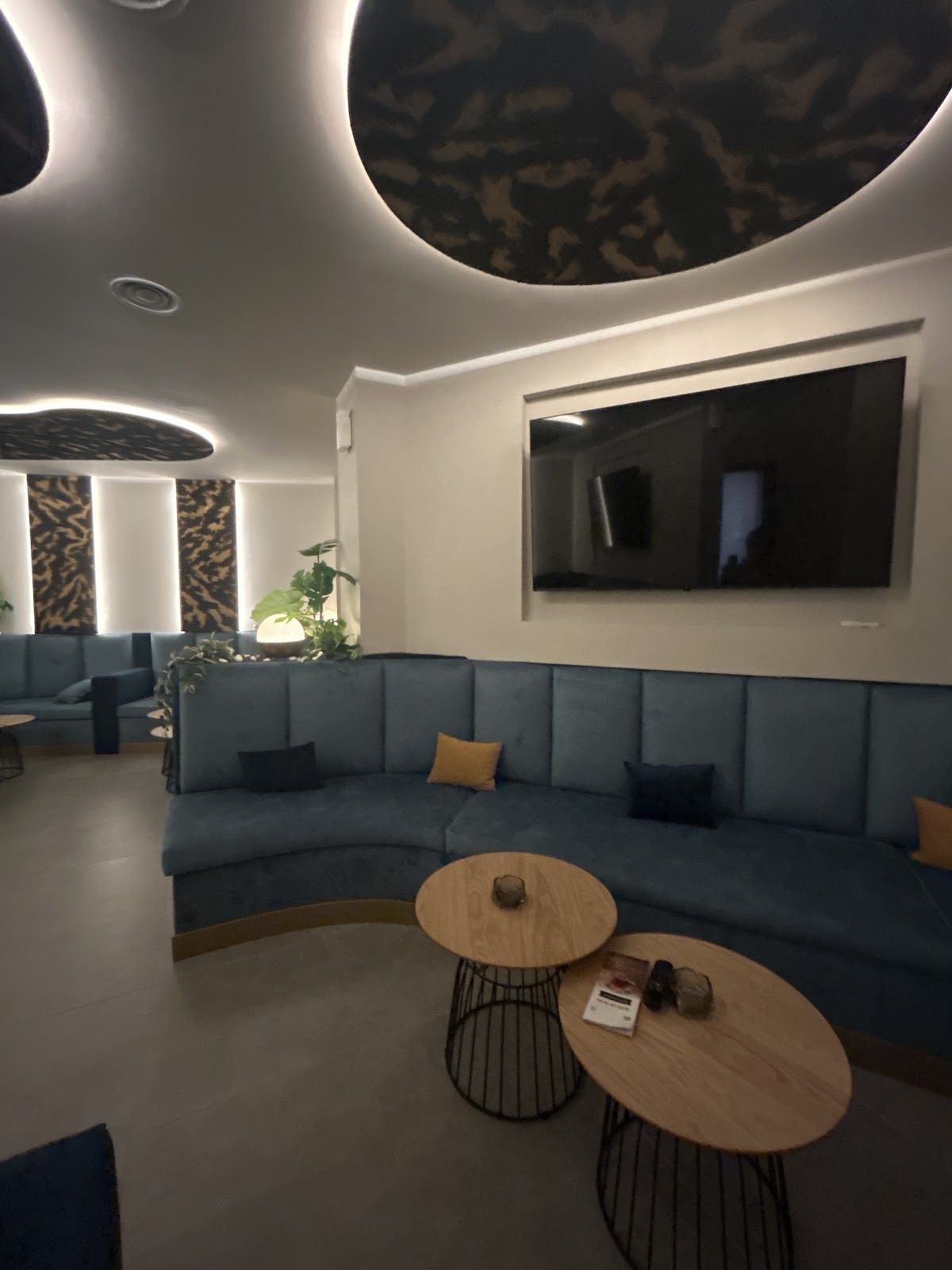 Interior de un acogedor club social con asientos azules, mesas de madera y una decoración moderna con iluminación tenue.