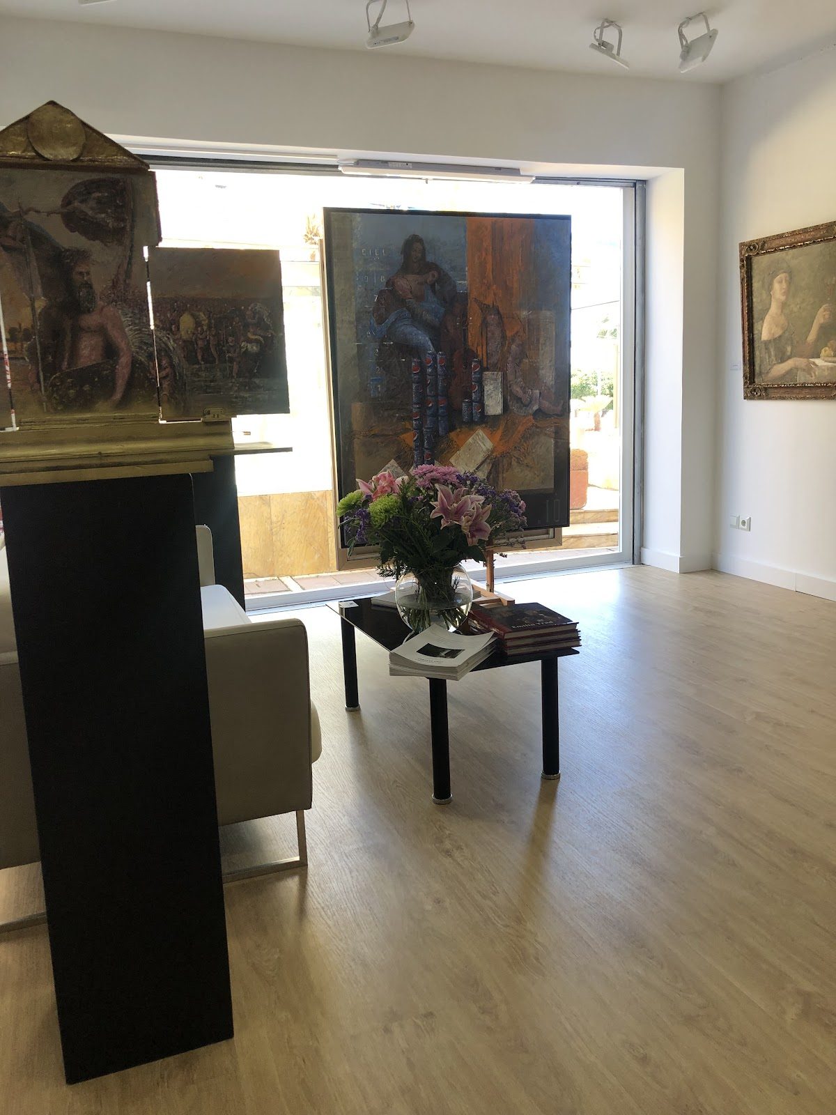 Interior de la galería D-art-A, con obras de arte, una zona de estar y un arreglo floral sobre una mesa.