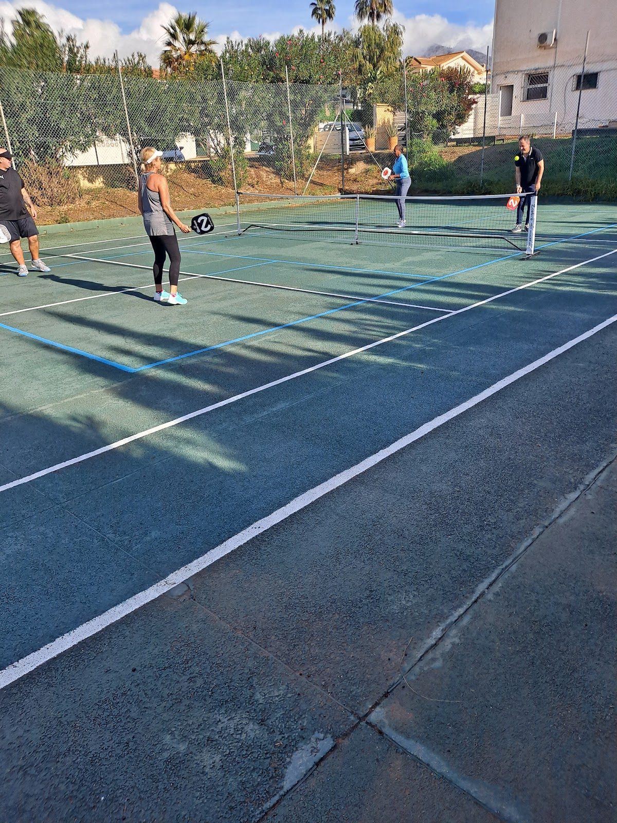 Jugadores participando en un partido de tenis en el Daryl Collins Algarrobo Tennis & Country Club, en un entorno soleado al aire libre.