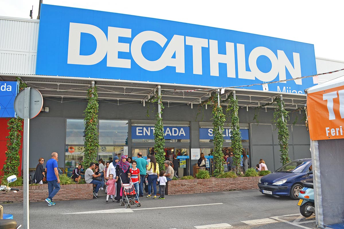 Decathlon Mijas cuenta con una gran fachada con gente entrando y saliendo, rodeada de vegetación.