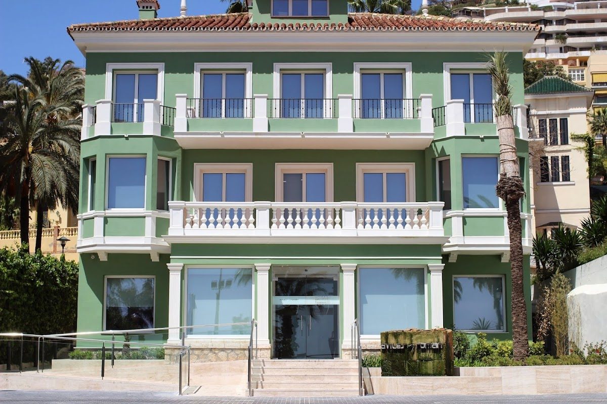 The Dental Clinic Aviles and Roman features a modern green building with large windows and a welcoming entrance.