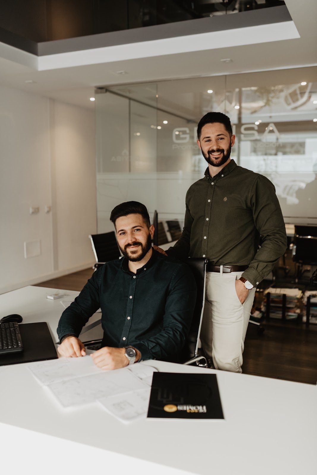 Two men in smart attire are working at a modern office desk at DeseaHomes in Nerja.