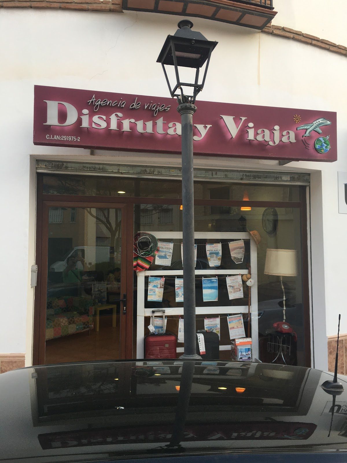 Exterior of Disfruta y Viaja travel agency with a lamp post and promotional materials in the window.