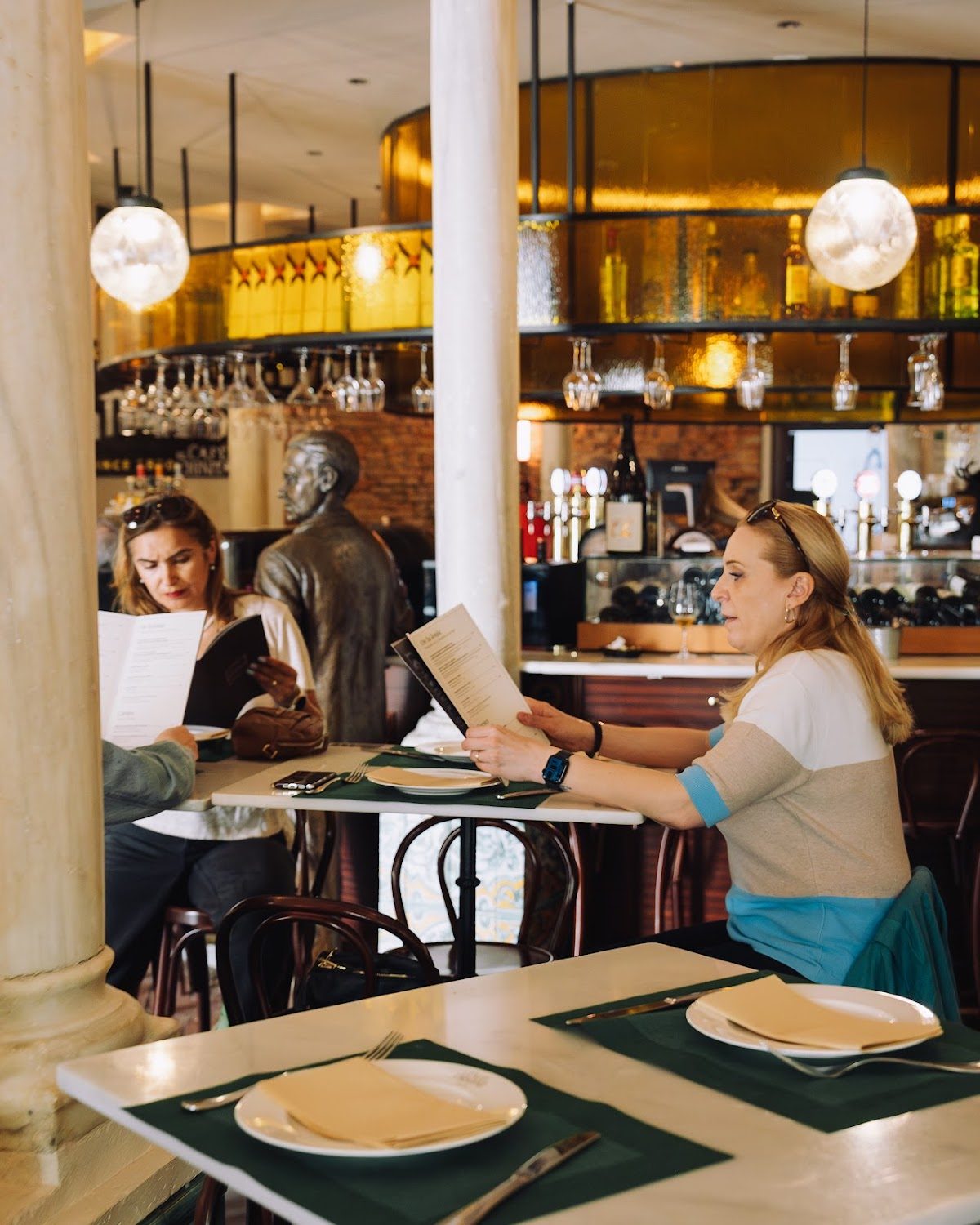 Interior de El Café de Chinitas con clientes leyendo los menús y una estatua al fondo.