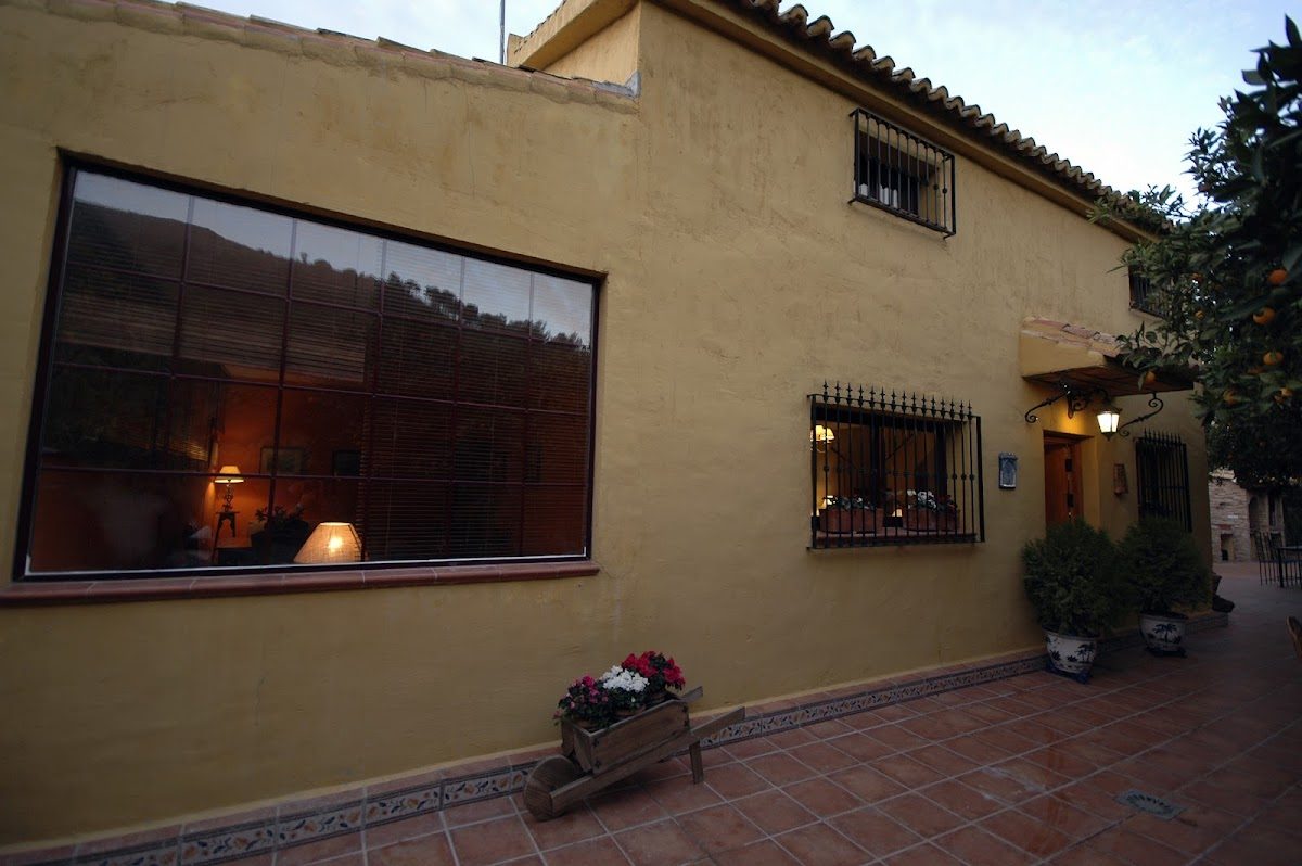 The exterior of El Capricho de Almadán features a yellow wall, large windows, and potted plants.