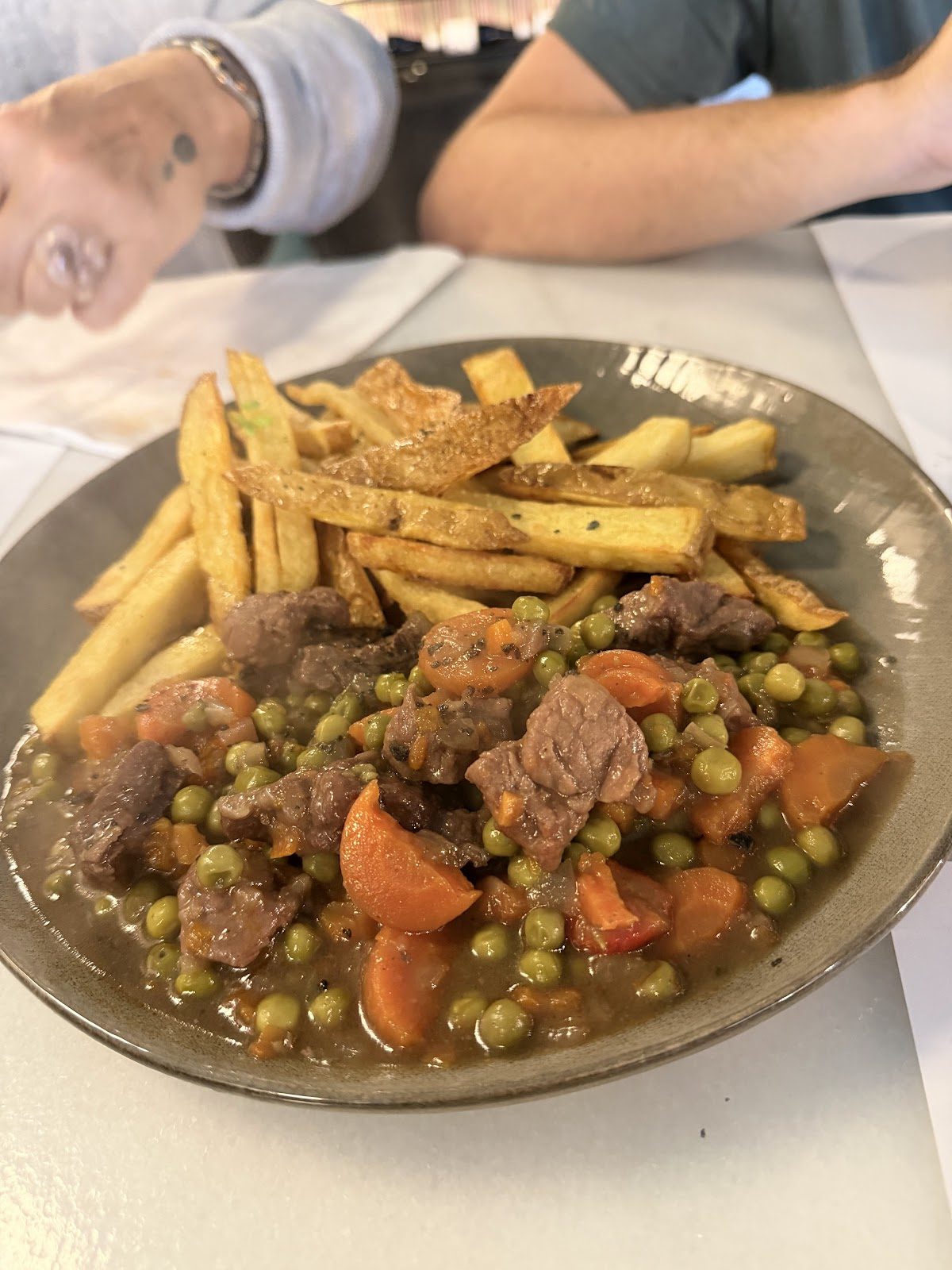 Un plato de estofado de ternera con guisantes y zanahorias, servido con patatas fritas doradas en El Fogón del Rubio Gastrotapas.