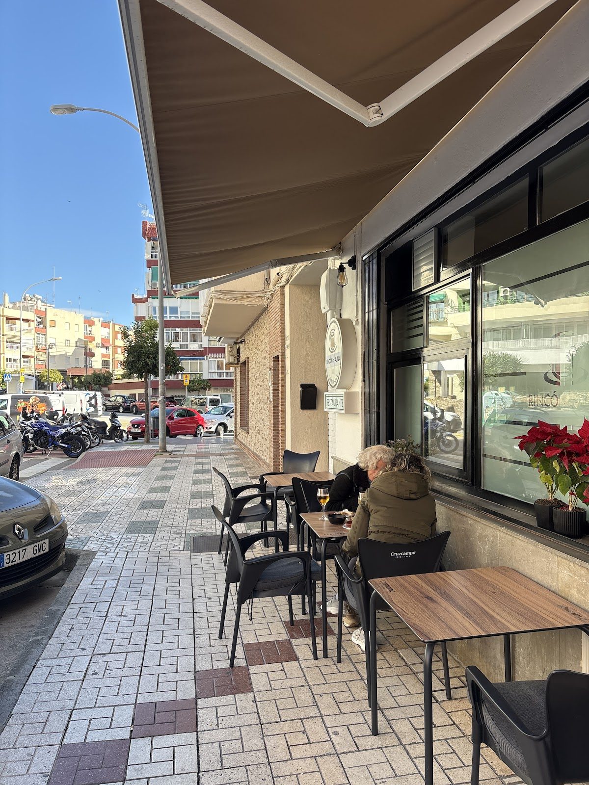 Outdoor seating area at El rincón Alina with patrons enjoying drinks on a sunny day.