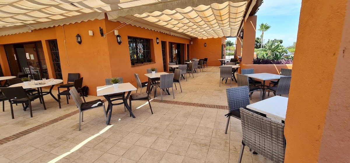 Outdoor seating area with white tables and wicker chairs at El Soto Restaurant in Ojén, Málaga.