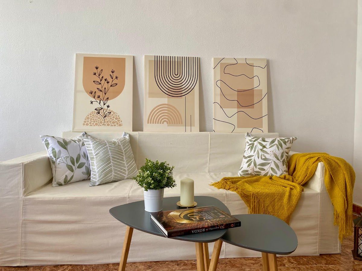Una acogedora sala de estar con un sofá blanco, cojines decorativos, una mesa de centro y arte moderno en las paredes.
