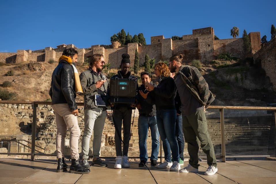 Un grupo de personas se reunió al aire libre, utilizando una cámara antigua con un castillo histórico de fondo.