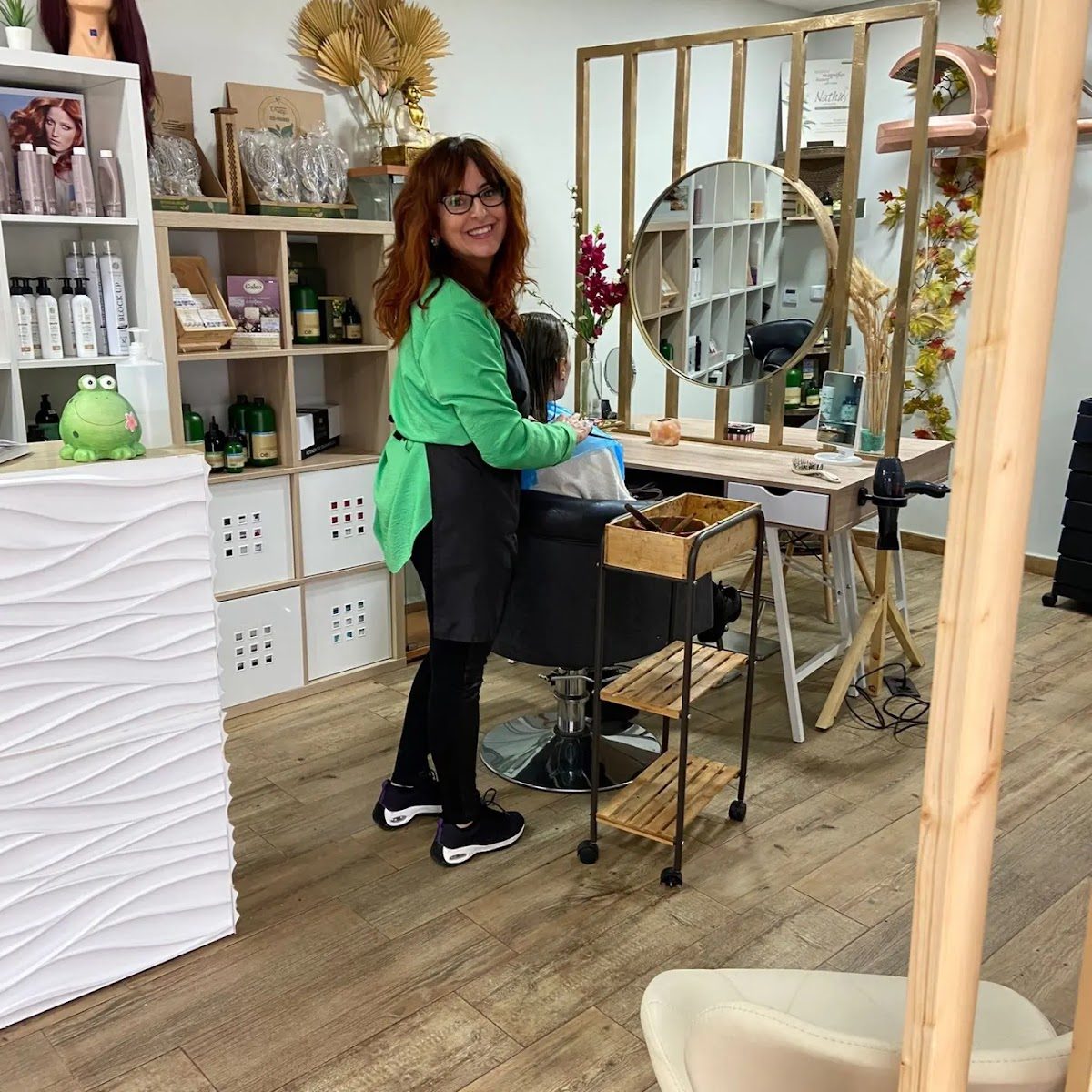 A stylist in a green shirt works at a hair salon with modern decor and a mirror.