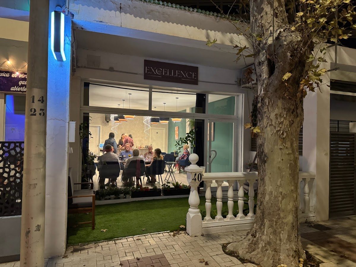 El exterior del restaurante Excellence: Gastronomic Restaurant presenta una entrada acogedora con un césped verde y mesas al aire libre.
