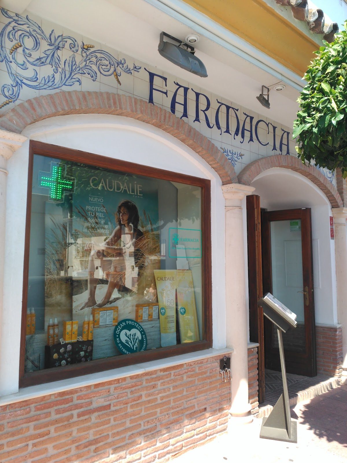 The exterior of Farmacia Benahavís CB features a window display with skincare products and a green cross sign.