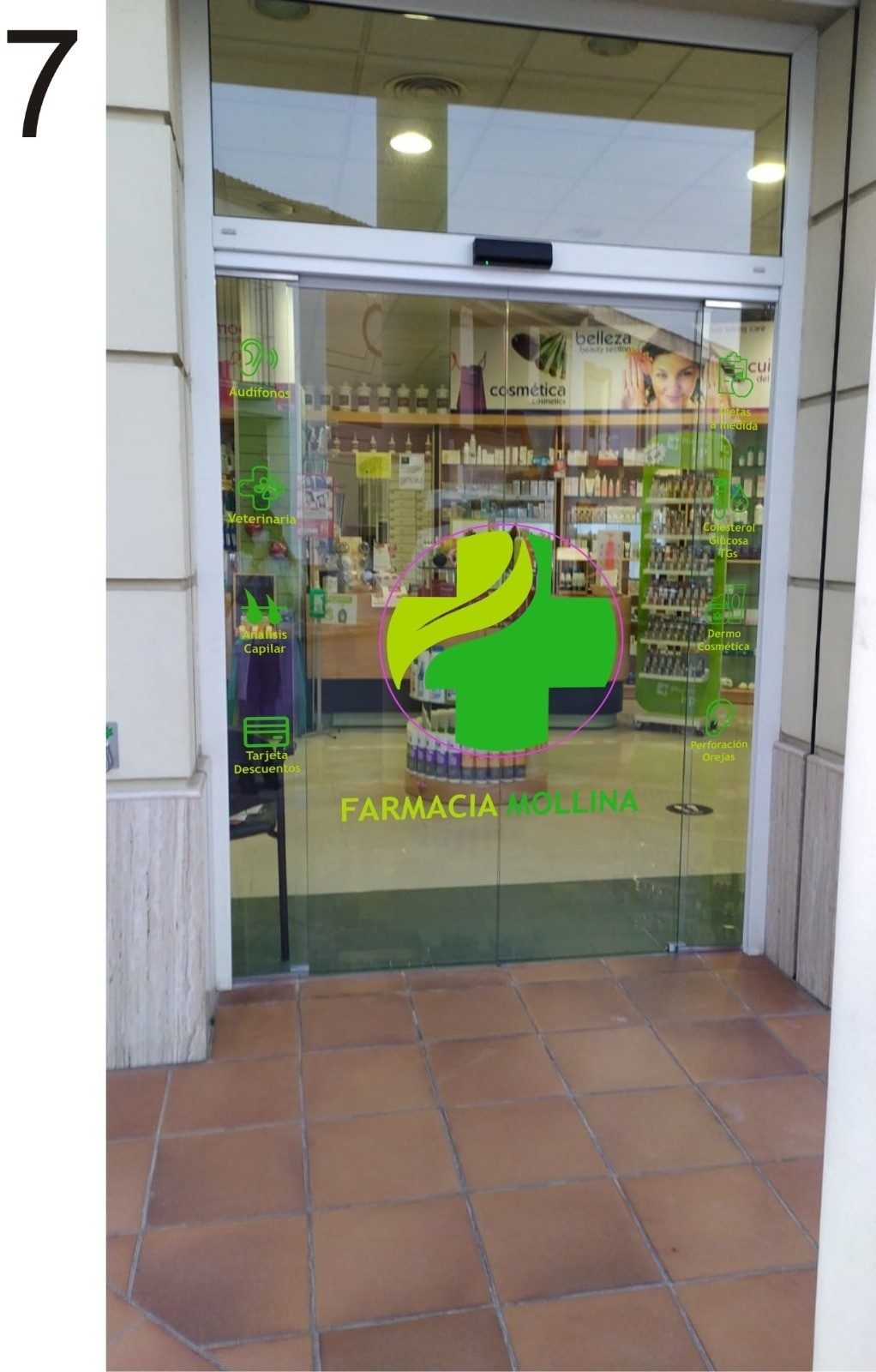 La entrada de Farmacia Mollina cuenta con una puerta de cristal con un logotipo verde y diversos productos farmacéuticos visibles en el interior.