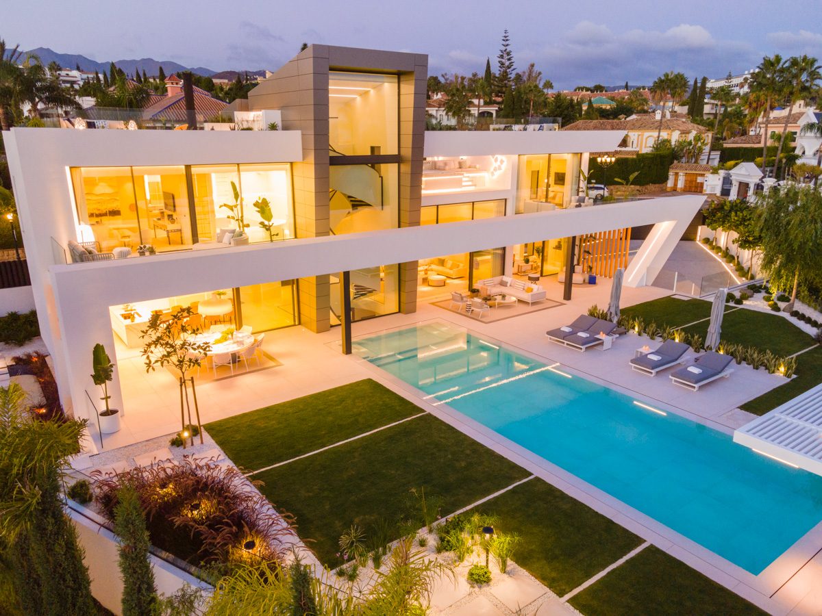 A modern villa with a large pool, landscaped garden, and stylish outdoor seating at Ferrari Estate Inmobiliaria.