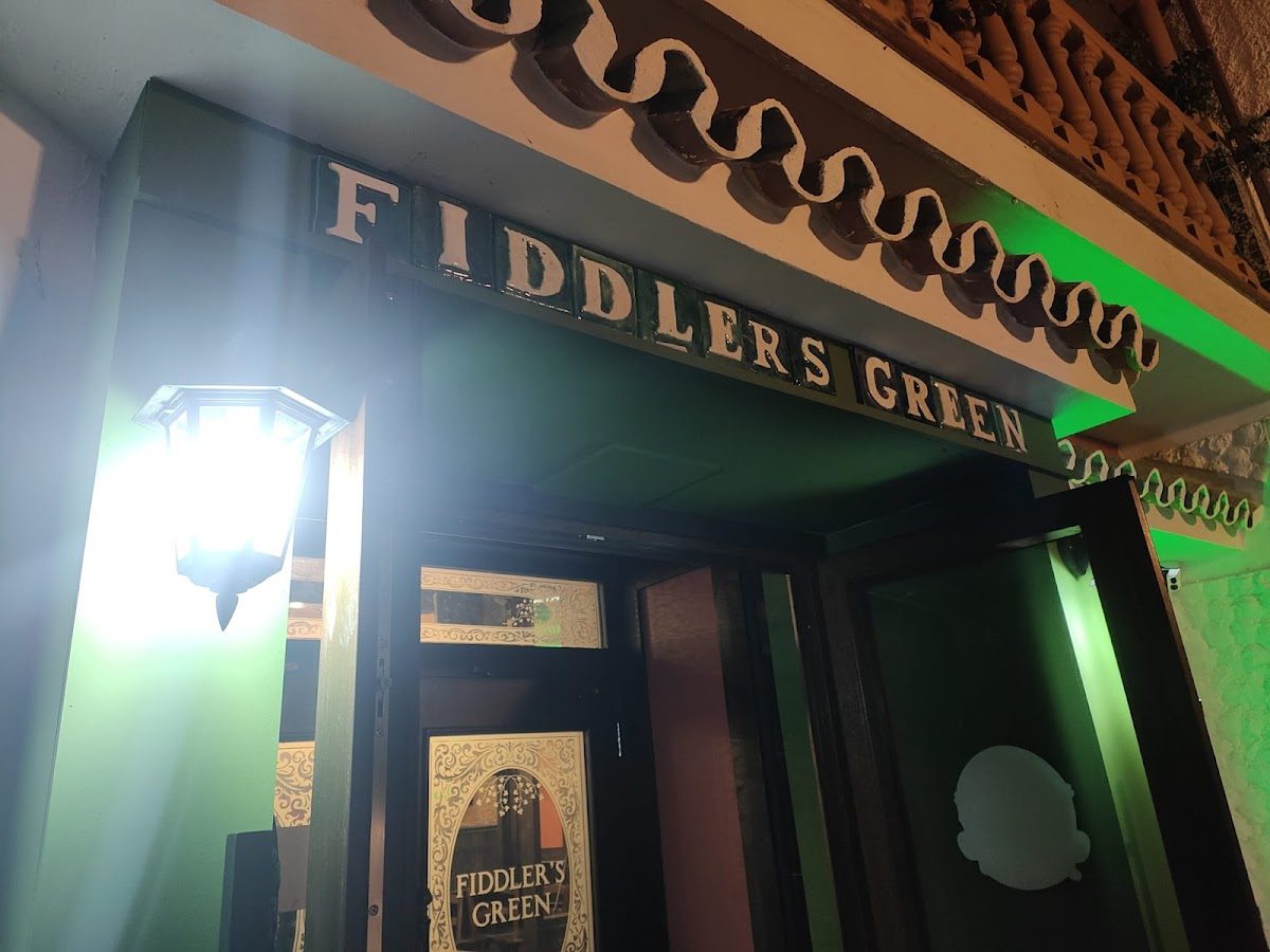 La entrada de Fiddler's Green presenta una fachada verde y letreros iluminados.