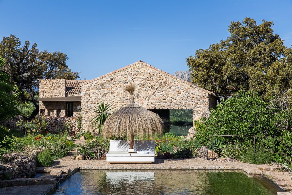 Finca La Donaira cuenta con un edificio rústico de piedra rodeado de exuberante vegetación y un estanque tranquilo con una pérgola de paja.