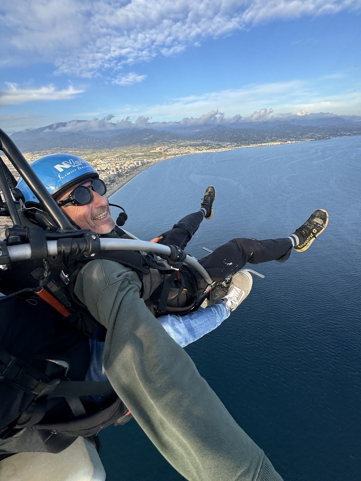 A person enjoying paragliding over the coastline, with stunning ocean views and a clear sky.