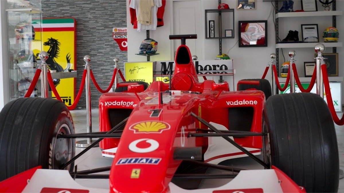 Un coche de carreras rojo se exhibía en un lugar destacado dentro del Formula Lounge, rodeado de cuerdas y objetos de colección.