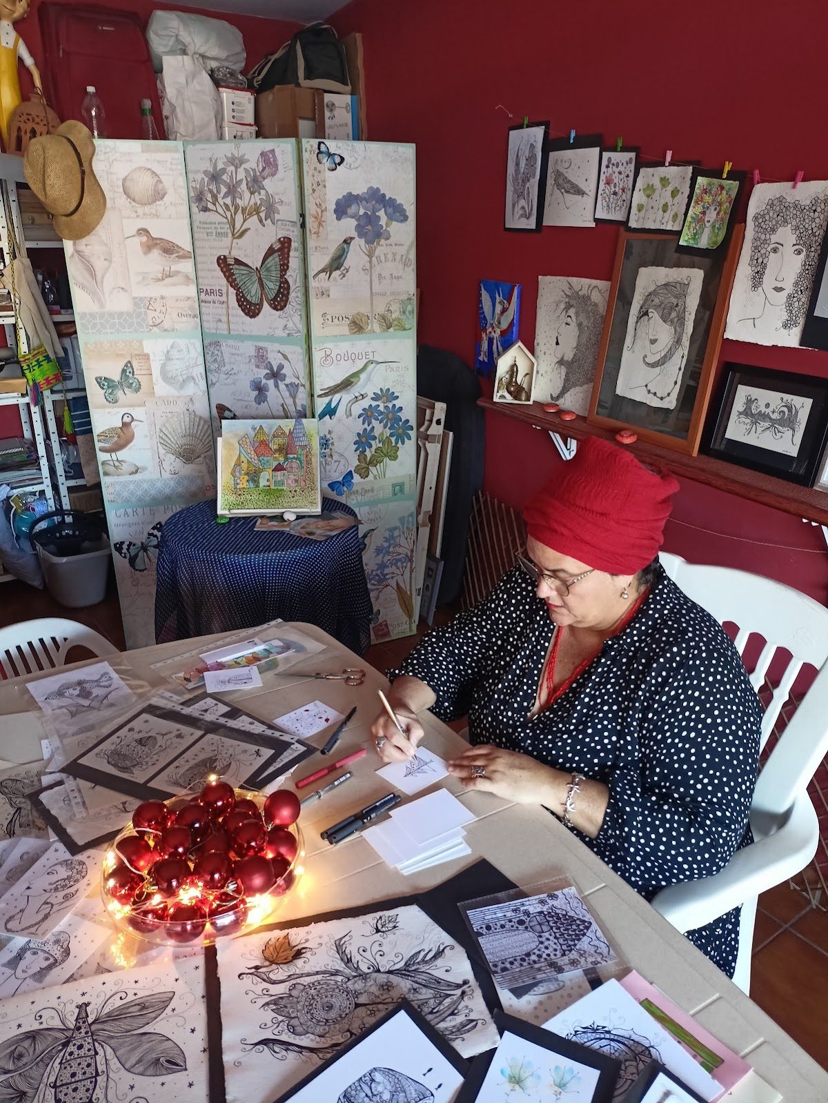 En la galería Garage, una mujer crea arte sentada a una mesa rodeada de dibujos y una colorida exposición.