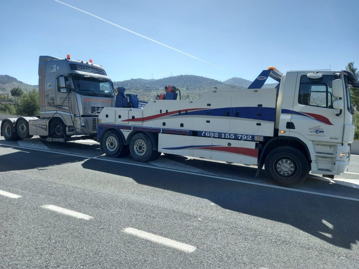 A tow truck from Grúas y Asistencia Antequera assisting a large vehicle on the roadside.