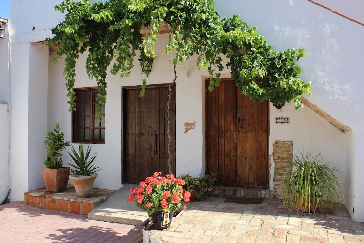 Charming exterior of Hacienda Horses featuring wooden doors, potted plants, and vibrant flowers.