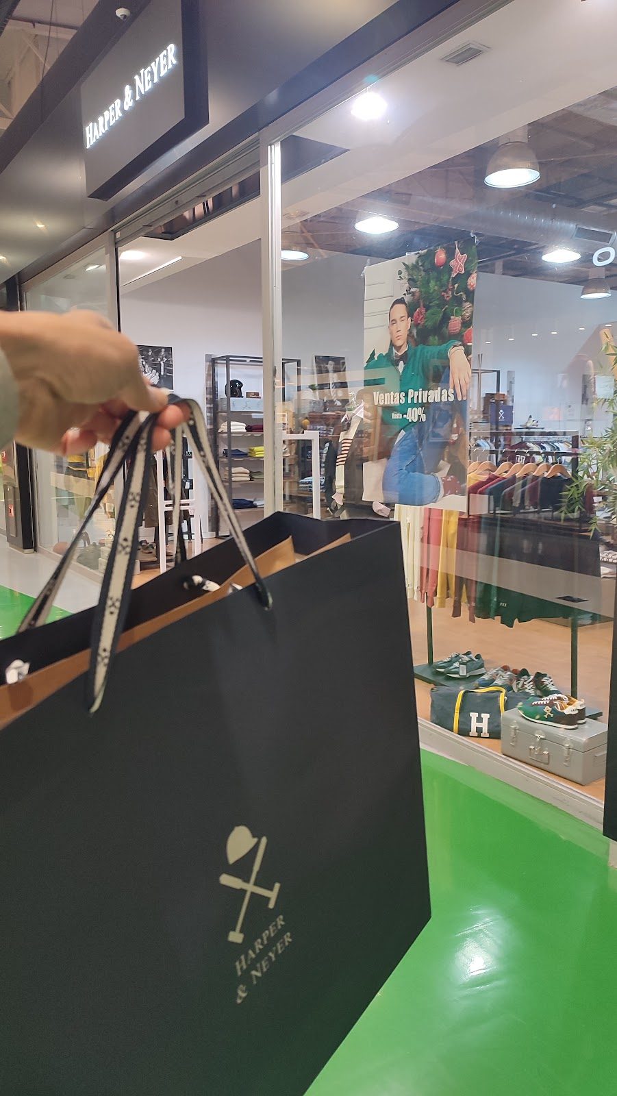A person holds a shopping bag in front of Harper & Neyer, showcasing a sale sign in the window.