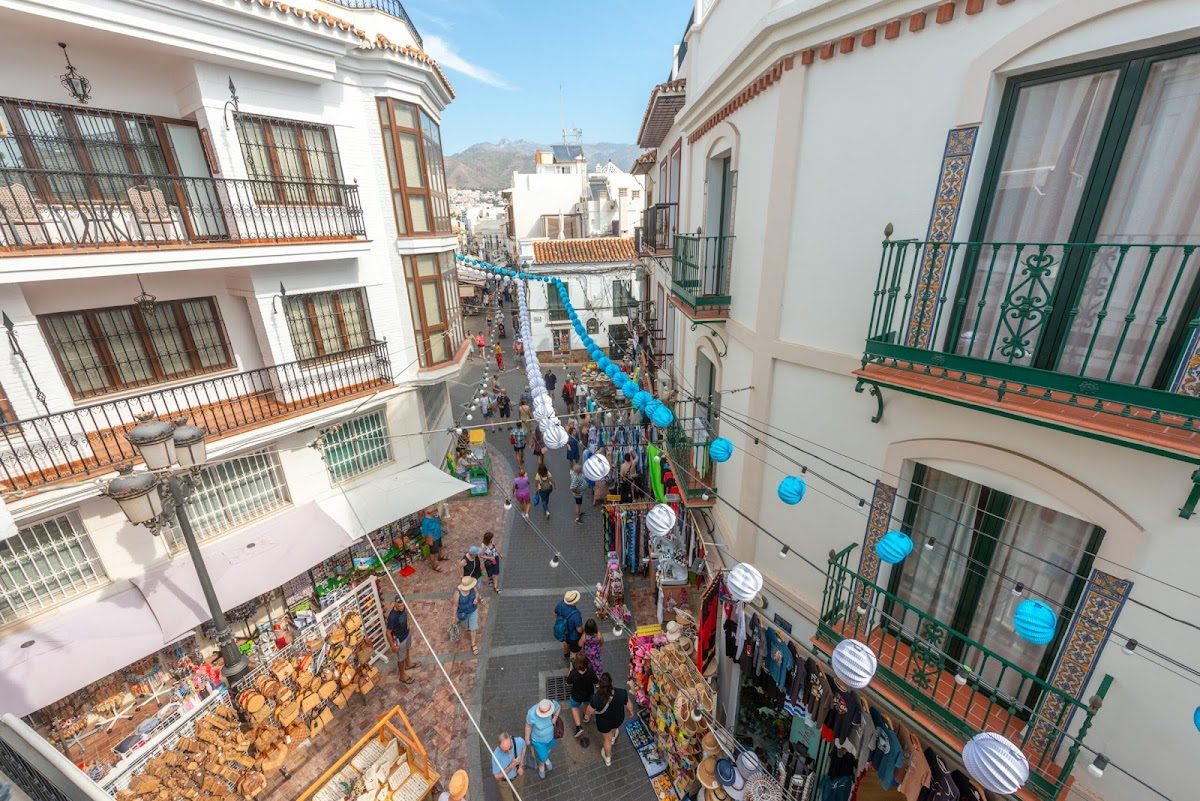 A vibrant street scene in Nerja with shops, decorations, and people enjoying the atmosphere near HC Calahonda Beach.