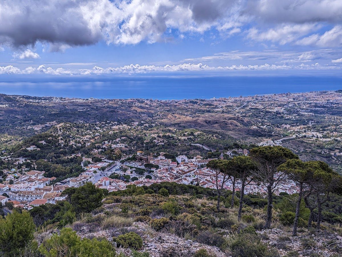 Vista panorámica de Mijas y la costa desde la Sierra de Mijas, con vegetación exuberante y cielos nublados.